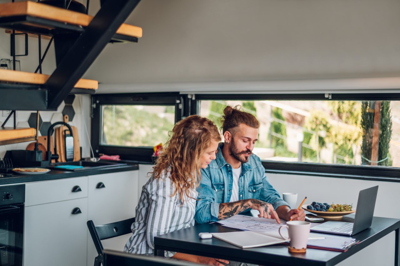 Happy couple using laptop and looking into blueprints of their new home